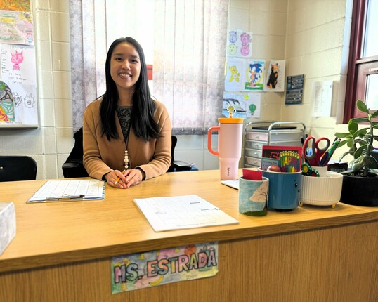 Ailee Estrada sits behind her desk smiling.
