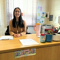 Ailee Estrada sits behind her desk smiling.