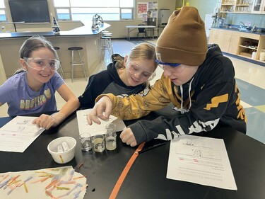 Three students at a table smiling doing a science experiment.